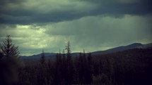 Timelapse of storm clouds moving over a tree-covered mountain range.