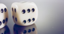 Slow motion panning macro shot of white dice on reflective surface.
