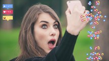 Girl taking selfies with animated social media emojis on either side of her.