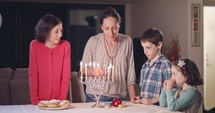 Kids and their mother lighting Hanukkah candles.