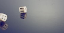 Slow motion macro shot of dice rolling on reflective surface.