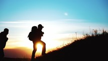 Silhouette tourists on hike with backpacks and equipment climbed on high mountain. Raise your hands up. Achieving set goal. Victory over yourself and great endurance and willpower. Sport lifestyle.