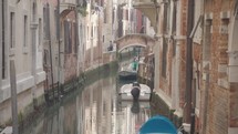 The atmosphere of narrow canals in the city of Venice, with many bridges and small boats parked.