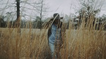 a woman walking through a field of tall grasses 