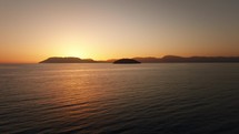 Aerial view above the sea during a scenic sunset with islands and mountains in the background, clear sky with no clouds