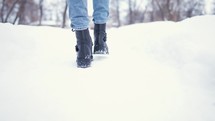 Close-up of female legs walking in winter snowy park. Woman walking in winter day. Black winter boots on legs. Active lifestyle at nature.