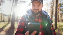 Young attractive man during the hike hold mobile phone, share message to friend distantly use social media network, watch received video, fun online concept. Technology and adventure concept.