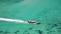 Wooden boat in turquoise sea, movement on blue water. Trip boat with tourists sailing on clean blue sea surface. A long-tailed Thai boat sails among the islands, touristic excursion ride. Aerial. 