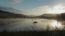 Fog rises from a small lake in the morning with sun behind