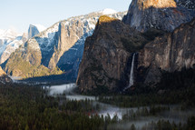 Snowy mountain in Yosemite with waterfall and foggy trees