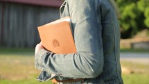 a woman walking caring a Bible on a farm 