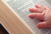 infants hand on the pages of a Bible