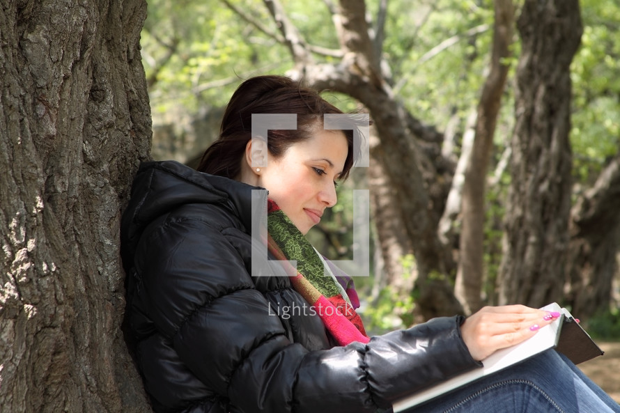 woman reading a Bible against a tree outdoors