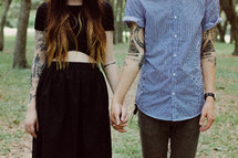 torso of a couple with tattoos holding hands 