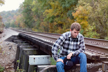 young man sitting on the train tracks 
