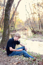 young man sitting by the edge of a creek 