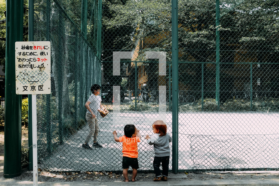 toddlers looking through a chain link fence 