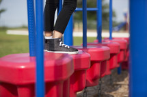 Legs and feet of a little girl playing on playground equipment.