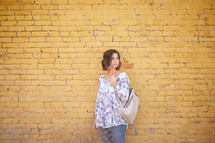 a woman standing in front of a yellow brick wall with her purse 
