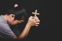 Close up of Asian woman's hands folded in prayer around a cross