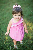 a toddler girl standing in green grass