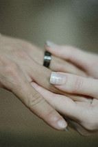 Woman's hand placing a ring on a man's finger.