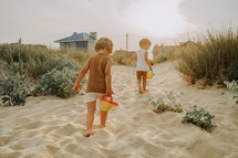 Cute unrecognizable little boys watering plants with cans on sandy beach. summer sunny day. Toddlers twins with colorful pots. Natural aestetic portrait of children. High quality photo