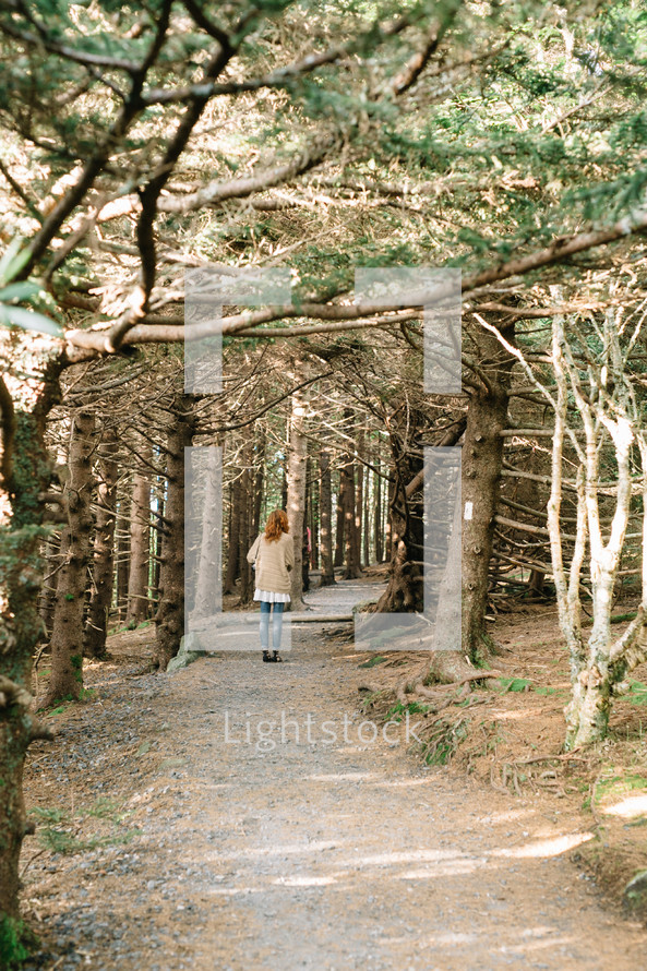a woman standing on a path in a forest 