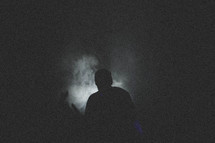 silhouette of a man standing in fog at night 