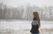 a young woman in a sweater standing in the snow 