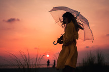a woman walking on a beach at sunset carrying an umbrella 