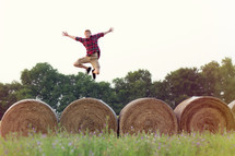 man leaping over hay bales 