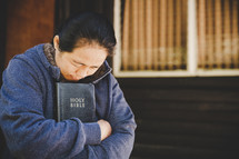 Asian woman with her Bible and eyes closed praying