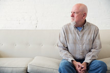 an elderly man sitting on a couch thinking 
