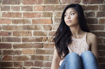 A pretty young woman sitting against a brick wall.