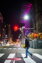 a man crossing a city street on a crosswalk at night 