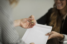 A smiling woman hands someone a blank pad and a pen.