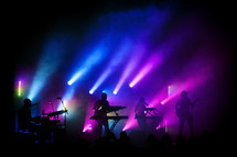 blue and purple stage lights on a band on stage at a concert 