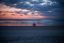 silhouette of a man on a bike on a beach at sunset 