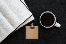 Bible, journal, notepad, clip, and coffee mug on a desk 