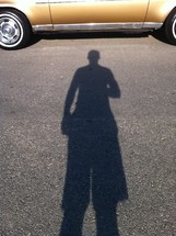 Boy's shadow on pavement in front of gold car.