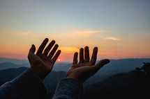 Hands outstretched in prayer at sunset