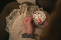 A woman with a cup of hot cocoa in her lap.