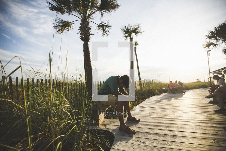 man sitting on a bench on a boardwalk praying 