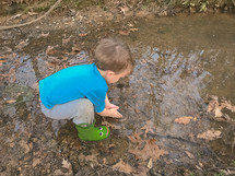 toddler boy in rain boots splashing in a puddle 