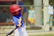 A young boy in little league swings and hits a baseball