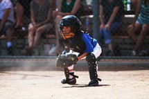 A young boy playing catcher at a little league baseball game