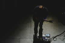 a musician on stage with guitar and foot pedals 