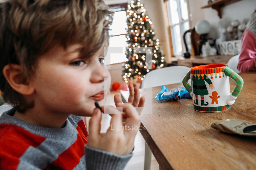 a kid sitting at a table with hot cocoa and eating at Christmas 