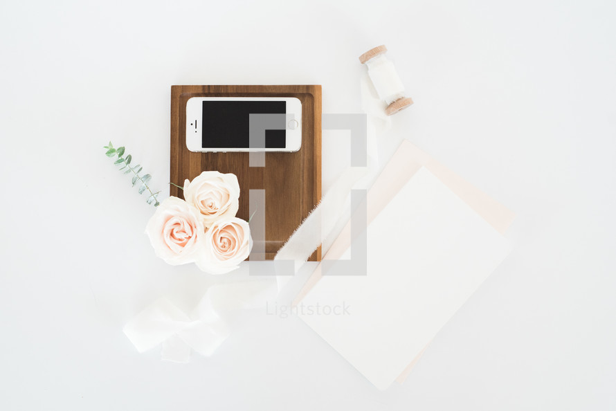 roses, cellphone, wood tray, spool of ribbons, and stationary 